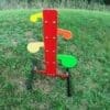 Colorful childrens playground climber with a red central post and yellow orange and green paddle like steps on metal legs on a grassy field