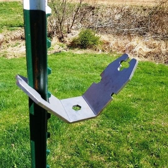 Metal bracket attached to a green post in a grassy yard, with two flat arms and circular holes in the metal.