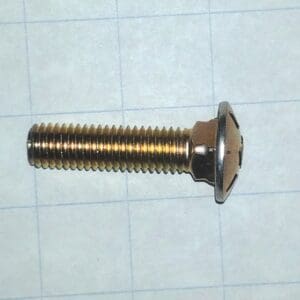 Metal bolt with a flanged round head and long threaded shank lying on graph paper likely a machine screw or shoulder bolt for mounting
