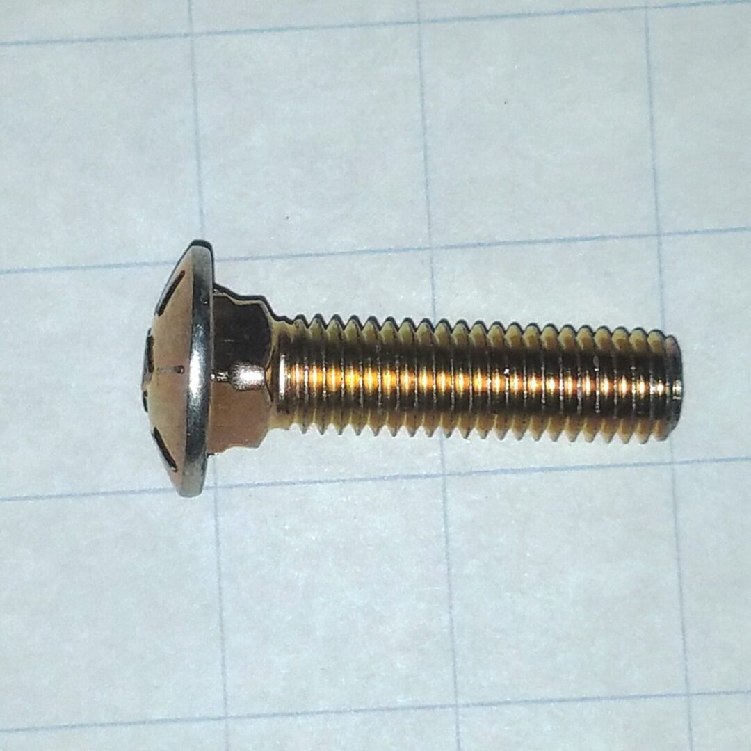 Metal bolt with a flanged round head and long threaded shank lying on graph paper likely a machine screw or shoulder bolt for mounting