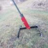 T Post stand 2 Hang Fast Targets Red metal plate attached to a black metal frame lying on grassy ground outdoors appears to be a disassembled piece of equipment or utility frame