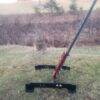 T Post stand 3 Hang Fast Targets Black metal A frame yard stand on grass with a red bracket attached to a long green pole outdoors in a field