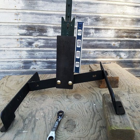T post stand 6 Hang Fast Targets Black metal frame jig with a vertical post and bubble level attached sits on a weathered wooden workbench with a wrench nearby
