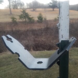 Metal bracket attached to a weathered white post extending outward to support a gate or fixture outdoors